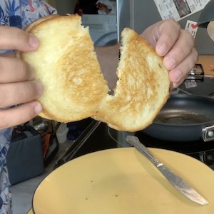 A finished grilled cheese sandwich is pulled apart to reveal melted cheese