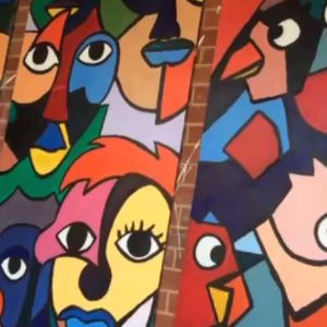 Banners of colorfully painted cubist faces hang in front of a brick wall