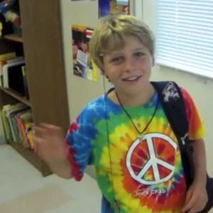 A young child wearing a tie dye shirt with a peace sign waves