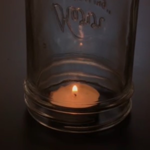 A tea candle sitting on a dark table is covered by a clear glass mason jar