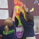 Two young students work together to pin a poster to the wall