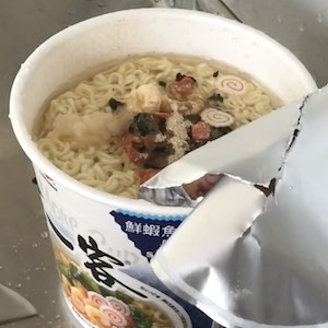 A cup of instant noodles, full of water, sits in a sink.