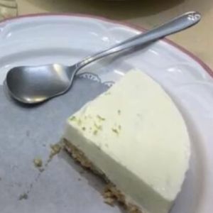 A quarter of a cheesecake sits on a plate with a spoon next to it