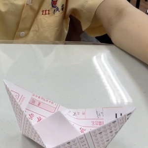 A finished paper boat sits on the table in front of the person who folded it