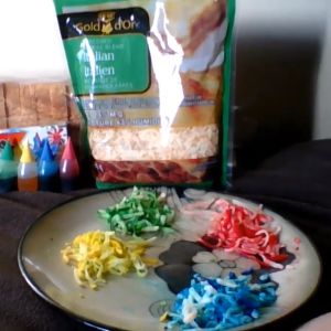 A bag of shredded cheese sits near different colors of cheese and food coloring.