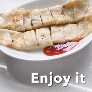 A finished and plated pancake is rolled and cut into pieces, with a red sauce on the side.