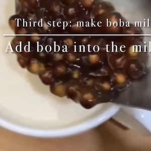 A spoon full of boiled boba bubbles is ready to drop them into a glass of tea.