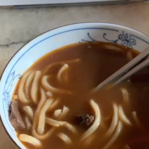 A ceramic soup bowl is filled with broth, beef, and noodles