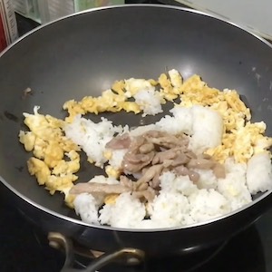 Eggs, rice, and pork sit in a wok on the stove.