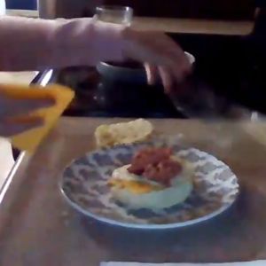 An egg sandwich sits on a plate with cheese about to be thrown on top.