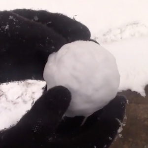 Dark mittens covered in snow hold a snowball