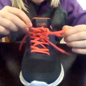 A close-up shot shows orange laces successfully tied on a black shoe.