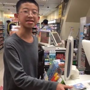 Someone stands at a cash register in a supermarket smiling as he hands his card to the clerk