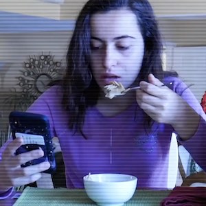 A young woman eats her breakfast cereal while staring at her phone nonstop