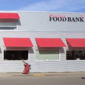 An exterior shot of the food bank shows a light colored building with bright red awnings