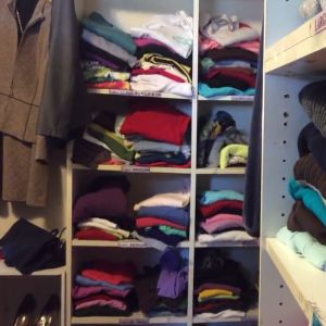 A closet organizer displays clothes of several different colors, folded or neatly hanging