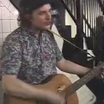 A man strums a guitar and sings near a stairway