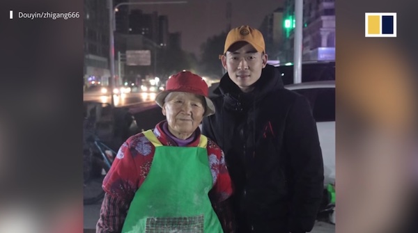 Elderly but lively lady smiles at the camera from behind a food cart.