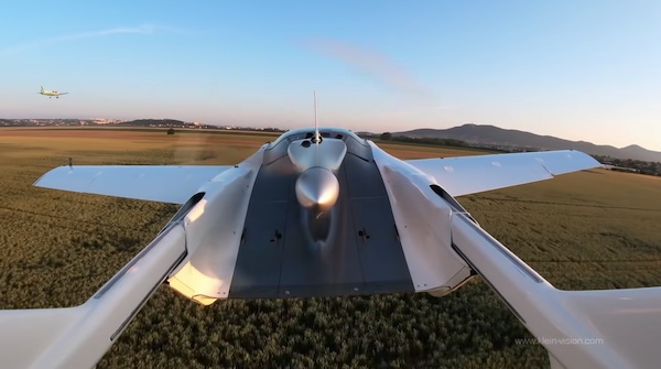 A car with wings flies above fields and a town