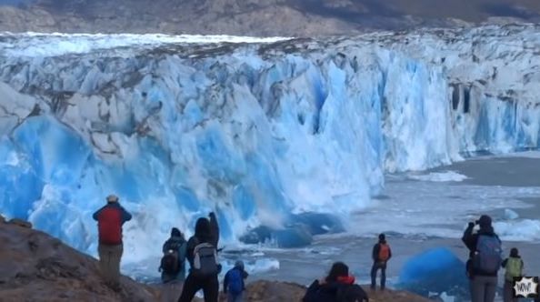 People watch as a glacier bursts and falls into the ocean