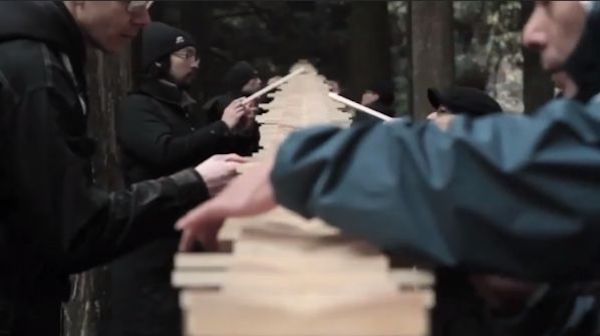 People in a forest carefully stack thin strips of wood