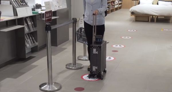 A small suitcase with what appears to be an attached camera is featured with all else fuzzy in the background. There is Japanese writing that translates as, 