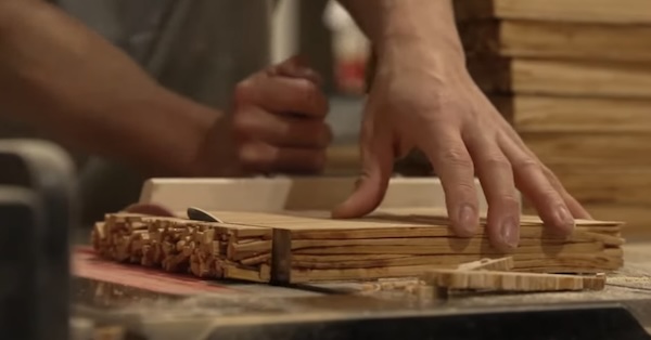 Old chopsticks being fused together to become material for something else. A hand guides the block of chopsticks toward a saw.