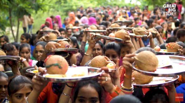 A crowd holds metal plates above their heads with coconuts and other items