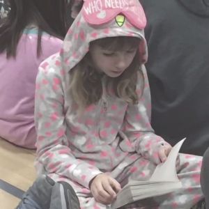 A young child sits on the ground with hooded pajamas, reading a book