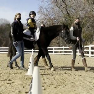 Two people assist in walking a horse that a child is sitting on