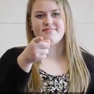 A blonde woman smiles and points straight at the camera