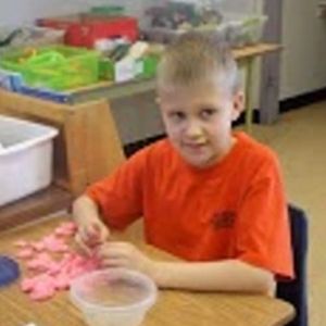 A young child sits at a table playing with Play-Doh