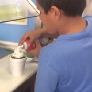 A person puts whipped cream on top of something in a styrofoam cup