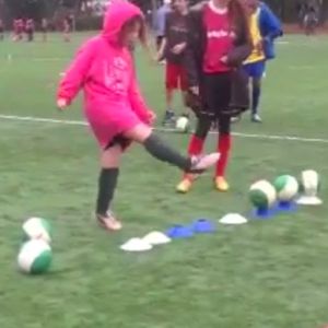 A young person kicks soccer balls to warm up during practice