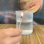 A hand holds a lit match in front of a cup of water with an image of a planet in the solar system in the background